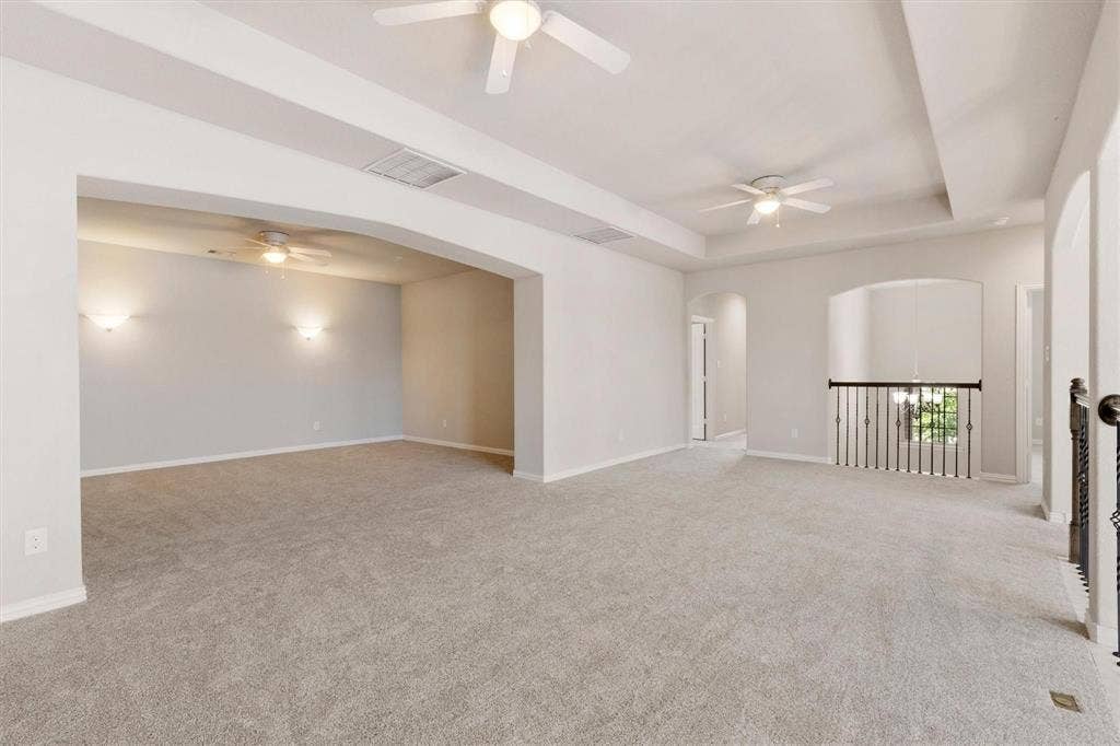4109 Rainey Street, McKinney, TX 75070 Expansive room featuring recessed tray ceilings, neutral carpeting, three ceiling fans, arched entryways, and decorative metal balusters
