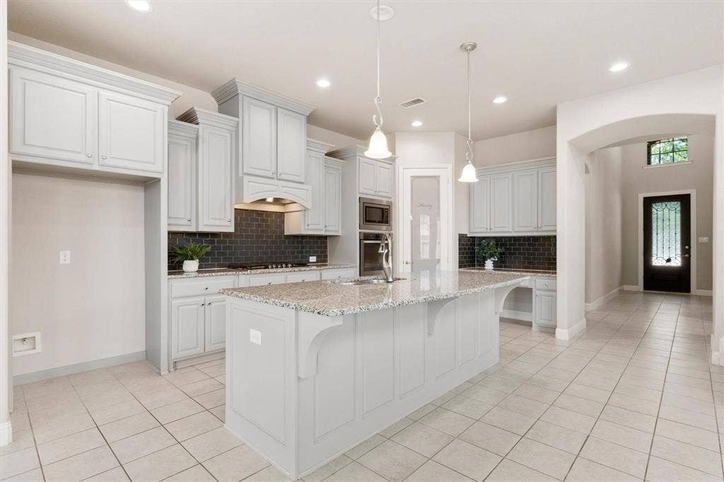 4109 Rainey Street, McKinney, TX 75070 Kitchen featuring light-toned cabinetry, a spacious stone-topped island, dark subway-tile backsplash, built-in double wall ovens, and recessed lighting