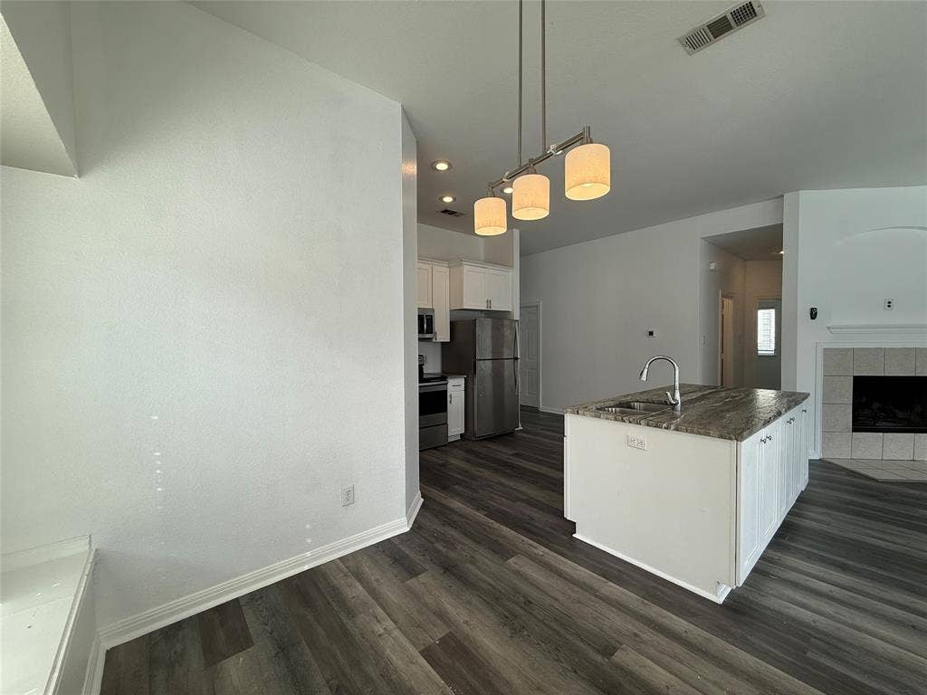 Kitchen featuring a stone-topped center island with a stainless steel faucet, wood-finish flooring, recessed lighting, and a three-bulb pendant fixture