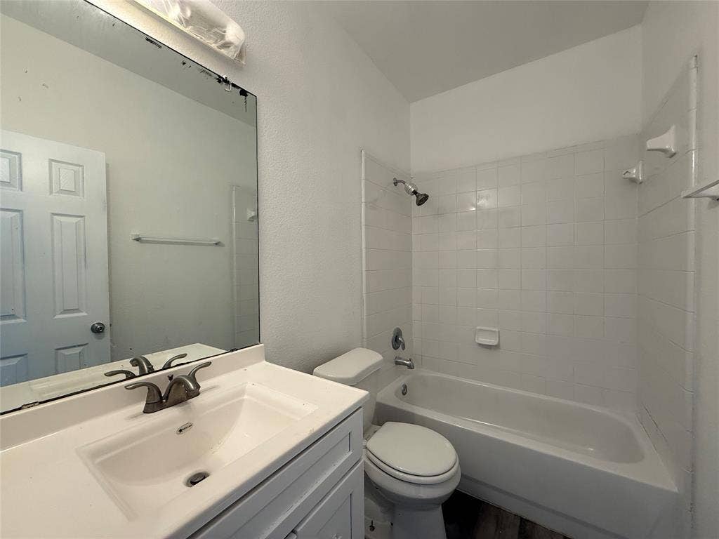 Bathroom featuring a white vanity cabinet, solid-surface countertop with an integrated sink, polished metal faucet, large wall-mounted mirror, and a tub-shower combination with white wall tile