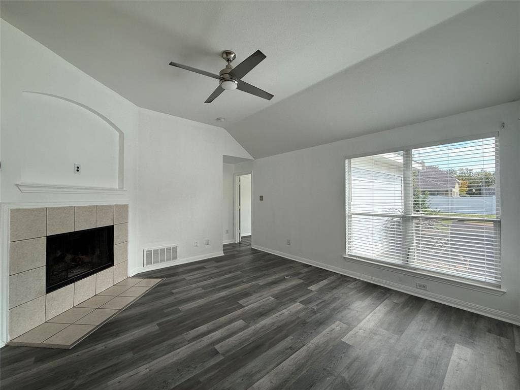 Vaulted ceilings, wood-finish flooring, corner fireplace with tile surround, and large window with blinds