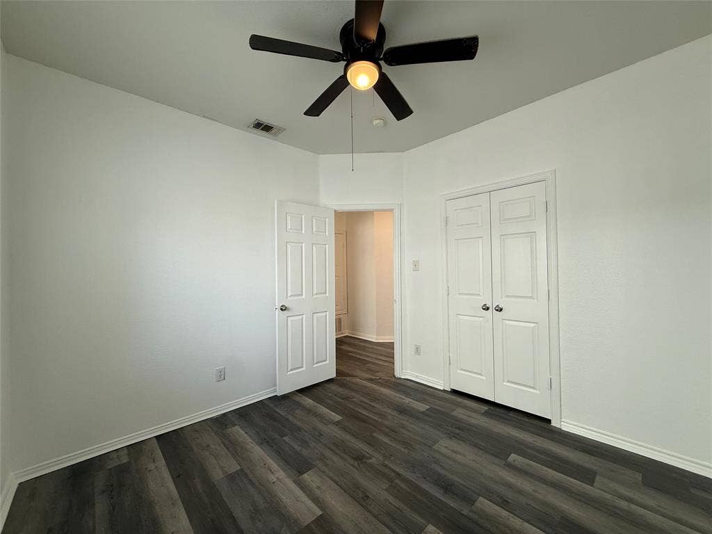 Room interior featuring wood-finish flooring, a multi-blade ceiling fan with integrated lighting, and dual-panel closet doors