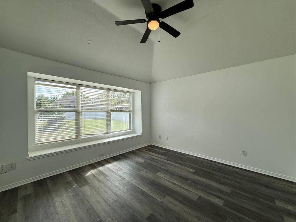 Vaulted ceiling featuring a central multi-blade ceiling fan, wide bay window with built-in ledge, and wood-finish flooring