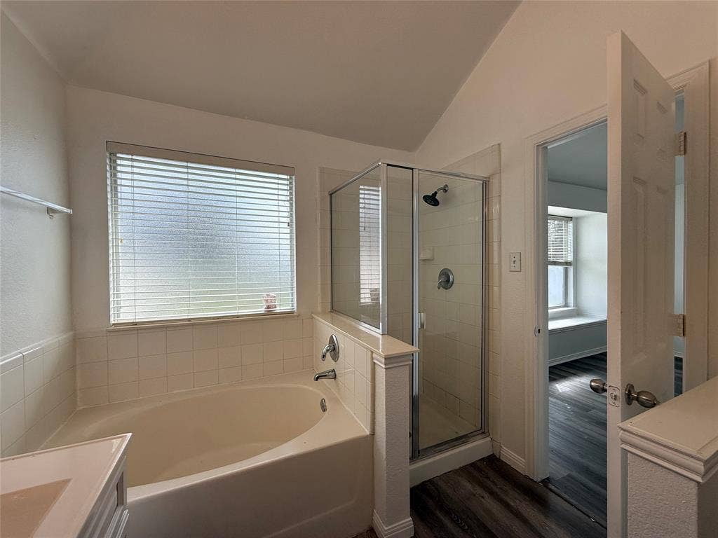 Soaking tub with tiled surround, glass-enclosed shower, sloped ceiling, and wood-finish flooring