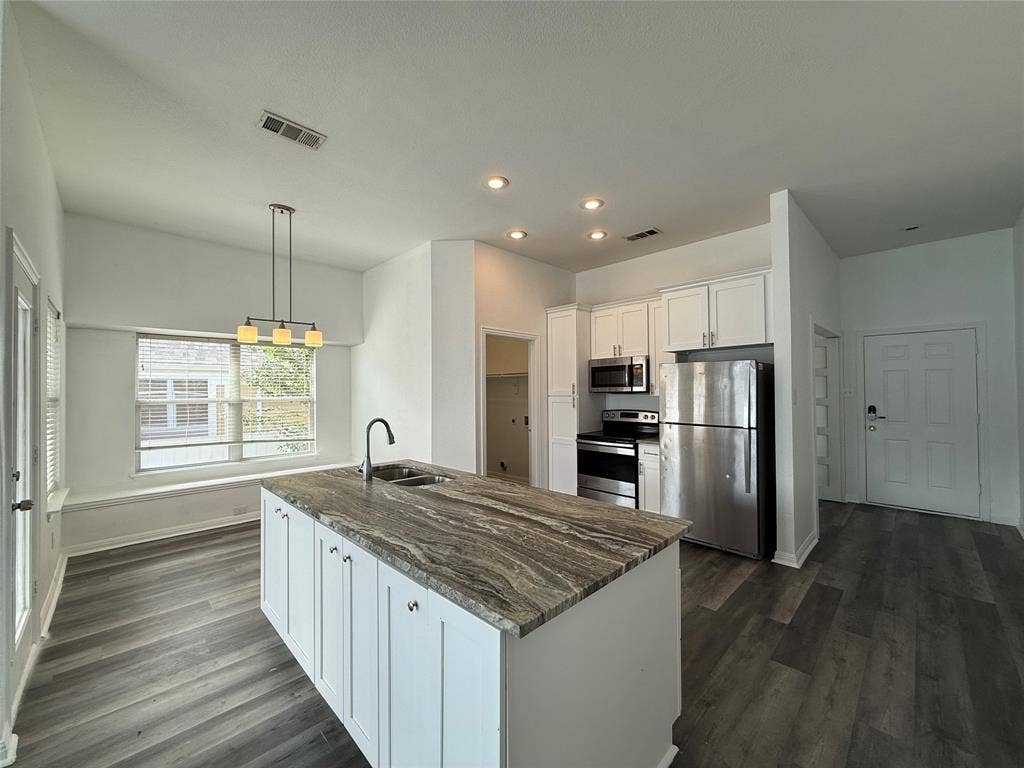 Kitchen featuring a stone-surface island, wood-finish flooring, white shaker-style cabinetry, stainless steel appliances, and a recessed window seat