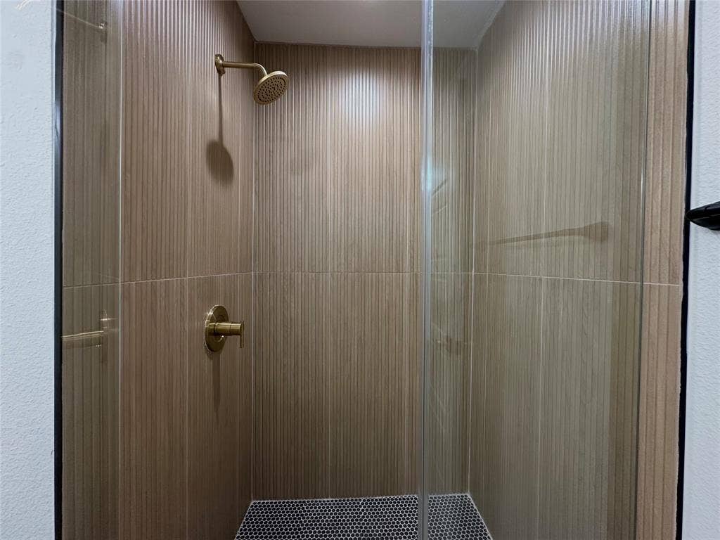 Shower enclosure featuring floor-to-ceiling vertical textured tile, hexagonal mosaic floor tile, brass-finish fixtures, and a glass door