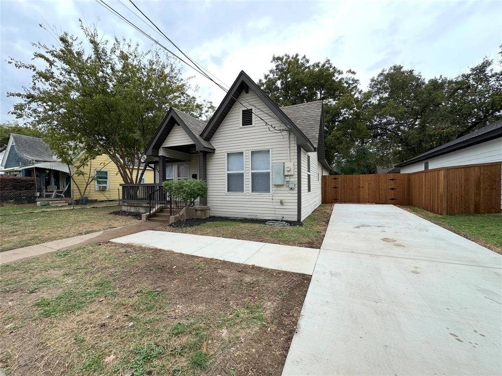 Exterior featuring light-colored horizontal siding, dual-gabled roofline, covered front porch, concrete driveway, and wood-panel privacy fencing