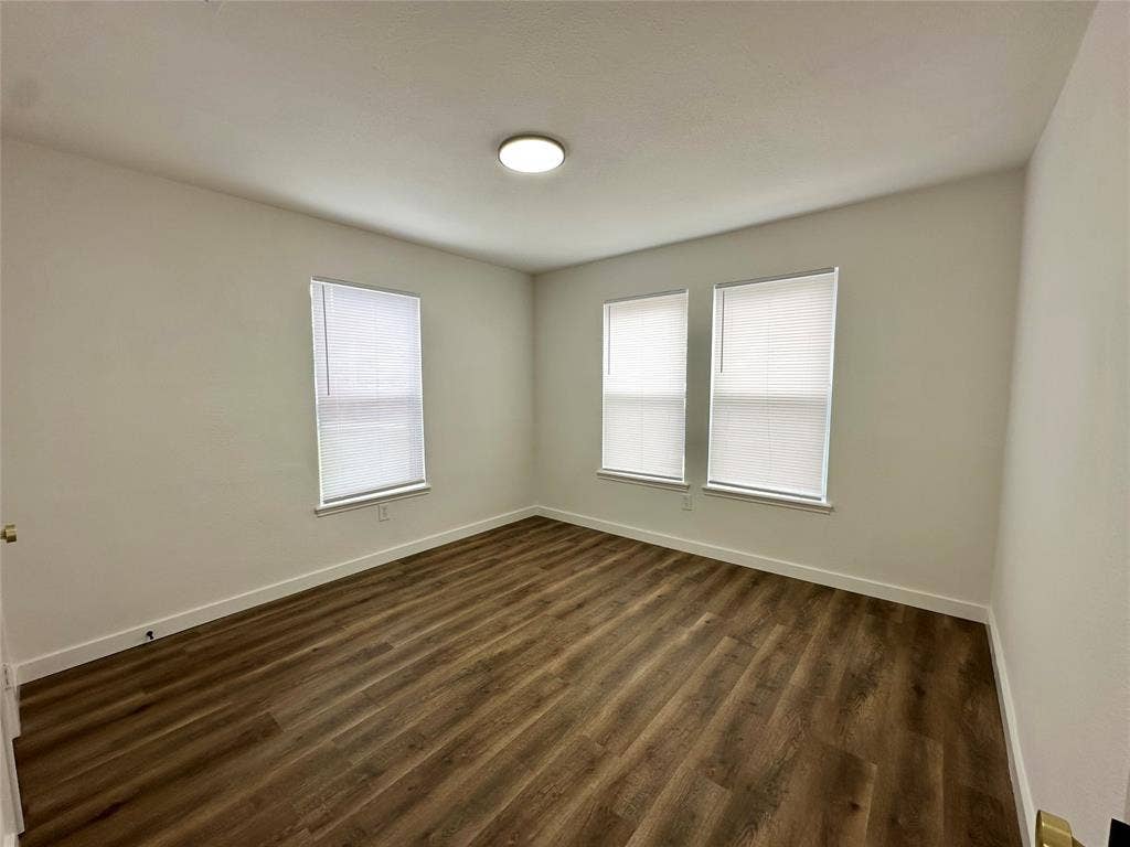 Room featuring wood-finish flooring, neutral wall tones, three windows with blinds, and a flush-mount ceiling light fixture