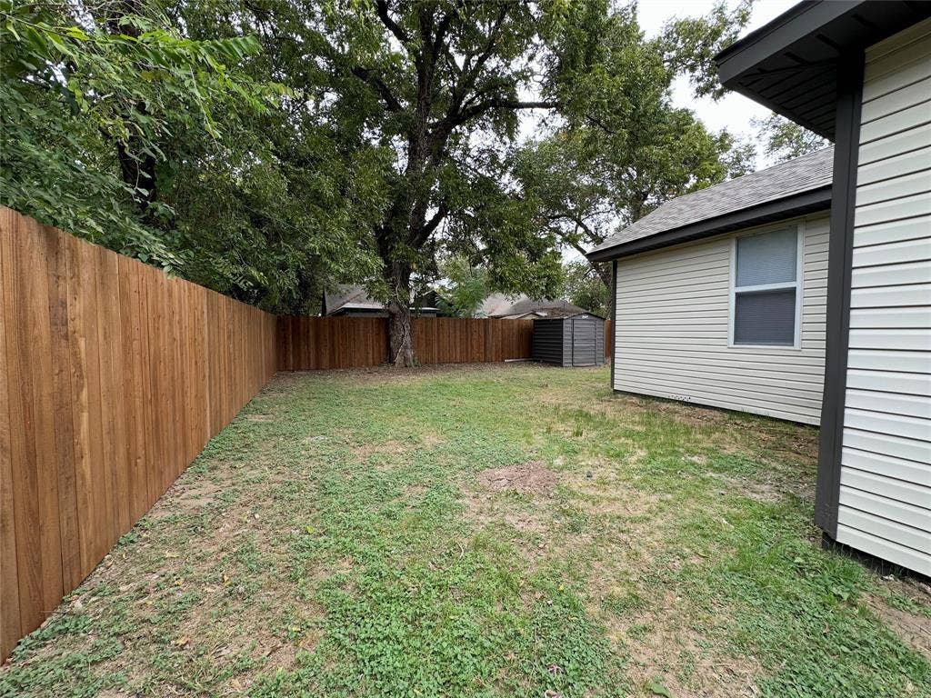 Backyard space featuring a horizontal wood privacy fence, vinyl siding exterior, and mature trees