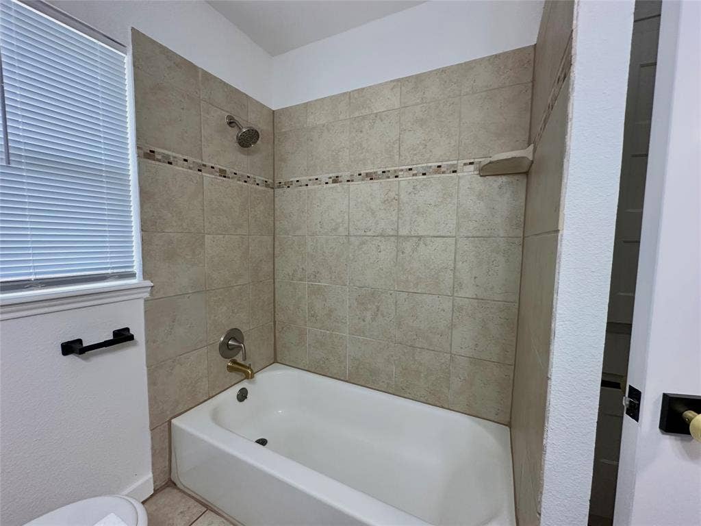 Bathtub surround featuring neutral ceramic wall tiling, a decorative glass mosaic accent border, a built-in recessed shelf, and metallic plumbing fixtures