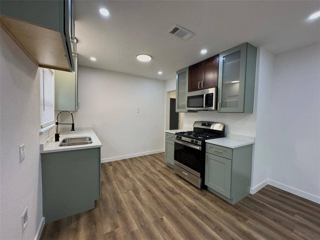 Kitchen featuring sage green cabinetry, stone-finish countertops, stainless steel gas range, integrated microwave, and wood-finish flooring