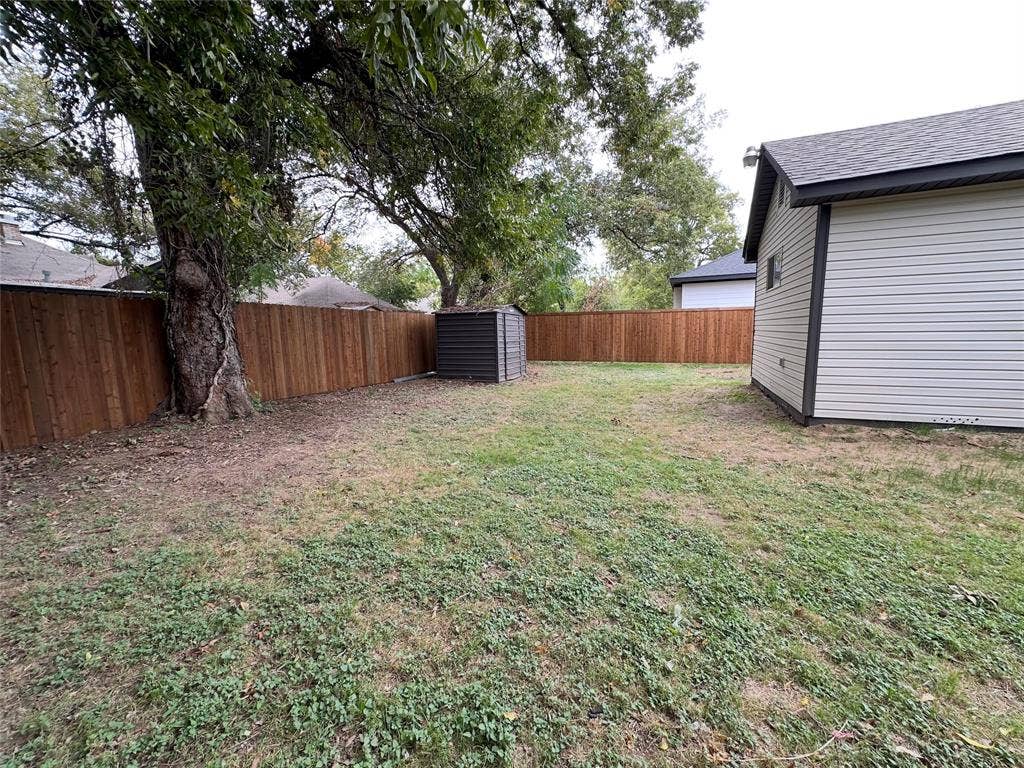 Backyard area featuring a wood fence, mature tree, standalone storage shed, and vinyl siding