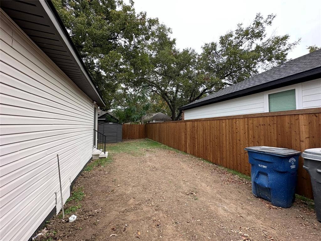 Side yard featuring light-colored horizontal siding, a tall stained-wood privacy fence, and mature trees