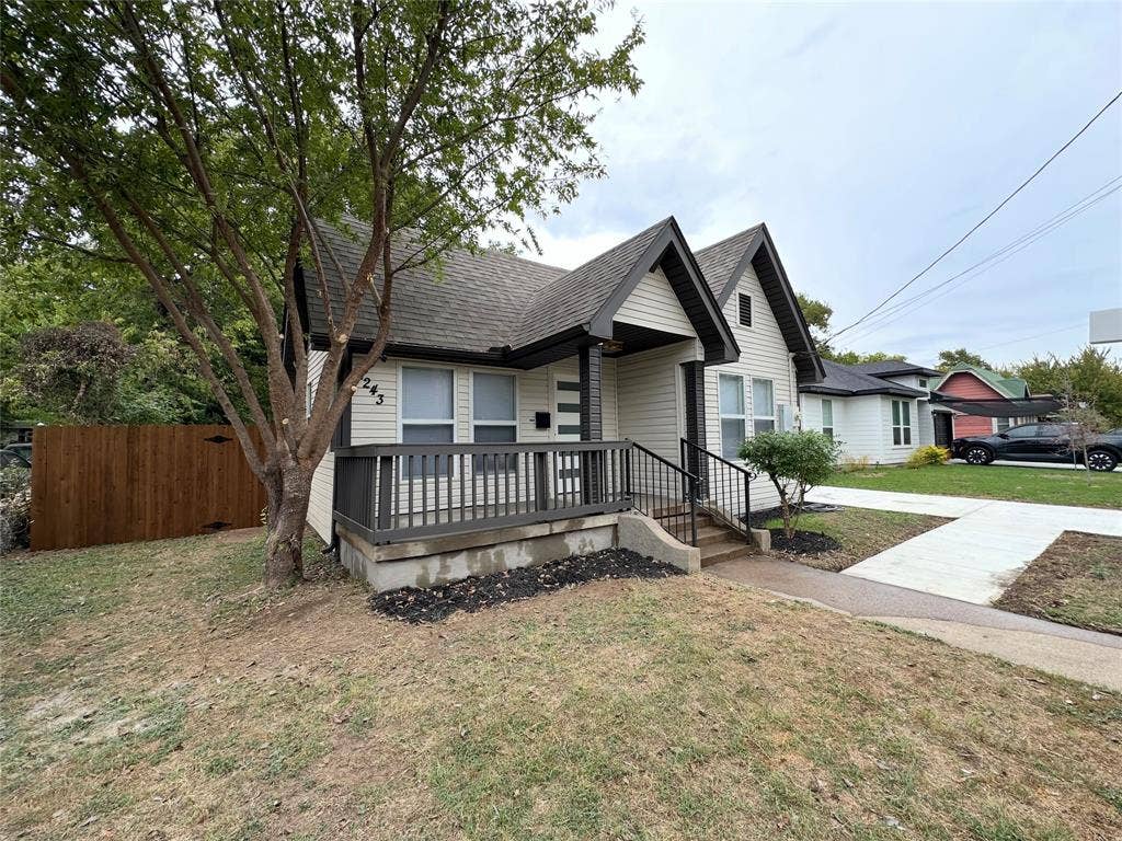 Exterior featuring light-toned horizontal siding, dual-gabled roofline, covered front porch with a dark railing, and a concrete driveway