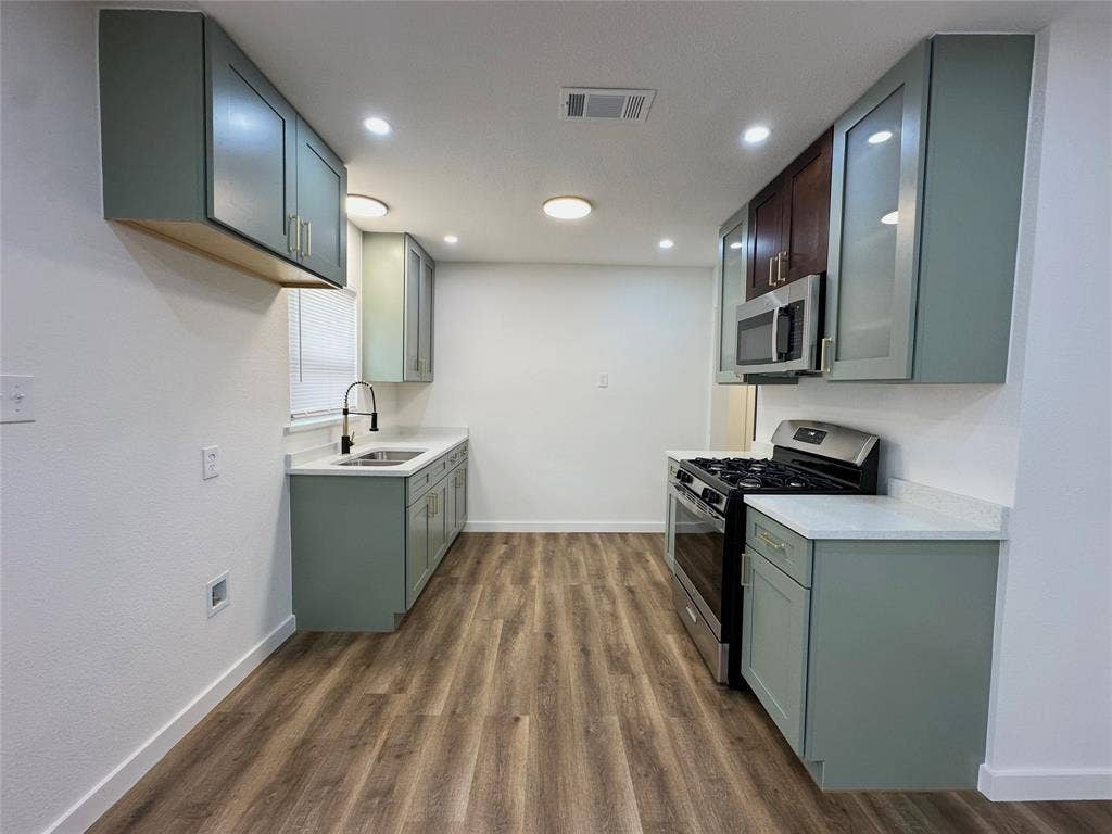 Kitchen featuring custom cabinetry with frosted glass inserts, stone-finish countertops, stainless steel appliances, wood-finish flooring, and recessed lighting