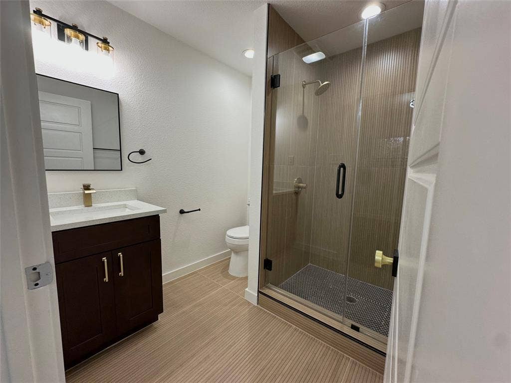 Bathroom featuring a dark wood-finish vanity with a light-toned countertop, a frameless glass-enclosed shower with floor-to-ceiling tile, and modern metallic fixtures