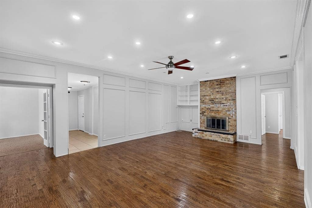 2413 Club Meadow Drive, Garland, TX 75041 Hardwood flooring throughout, featuring a brick-face fireplace with hearth, built-in shelving, recessed ceiling lighting, and crown molding