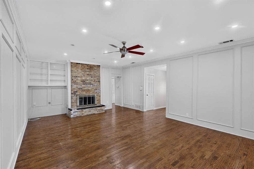 2413 Club Meadow Drive, Garland, TX 75041 Wood flooring, recessed lighting, brick fireplace with a black hearth, built-in shelving, and decorative wall paneling
