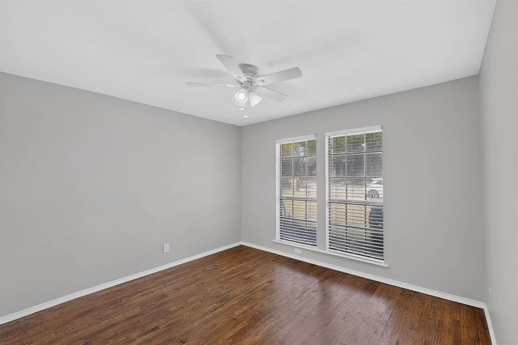 2413 Club Meadow Drive, Garland, TX 75041 Wood-finish flooring, light gray walls, white ceiling fan, and two large windows with blinds