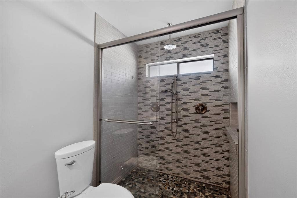2413 Club Meadow Drive, Garland, TX 75041 Glass-enclosed shower with a rain shower head, handheld shower, stone pebble flooring, and a tiled accent wall