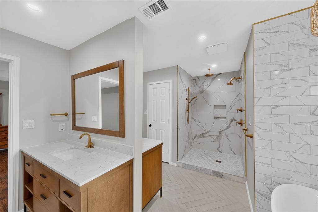 2413 Club Meadow Drive, Garland, TX 75041 Dual shower system, wood-finish double sided vanity with countertop, framed mirror, herringbone pattern flooring, and white tiled shower walls