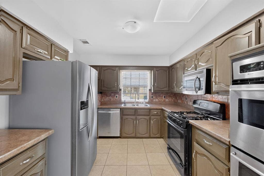 2413 Club Meadow Drive, Garland, TX 75041 Kitchen featuring wood-finish cabinetry, tile flooring, stainless steel appliances, and a built-in microwave