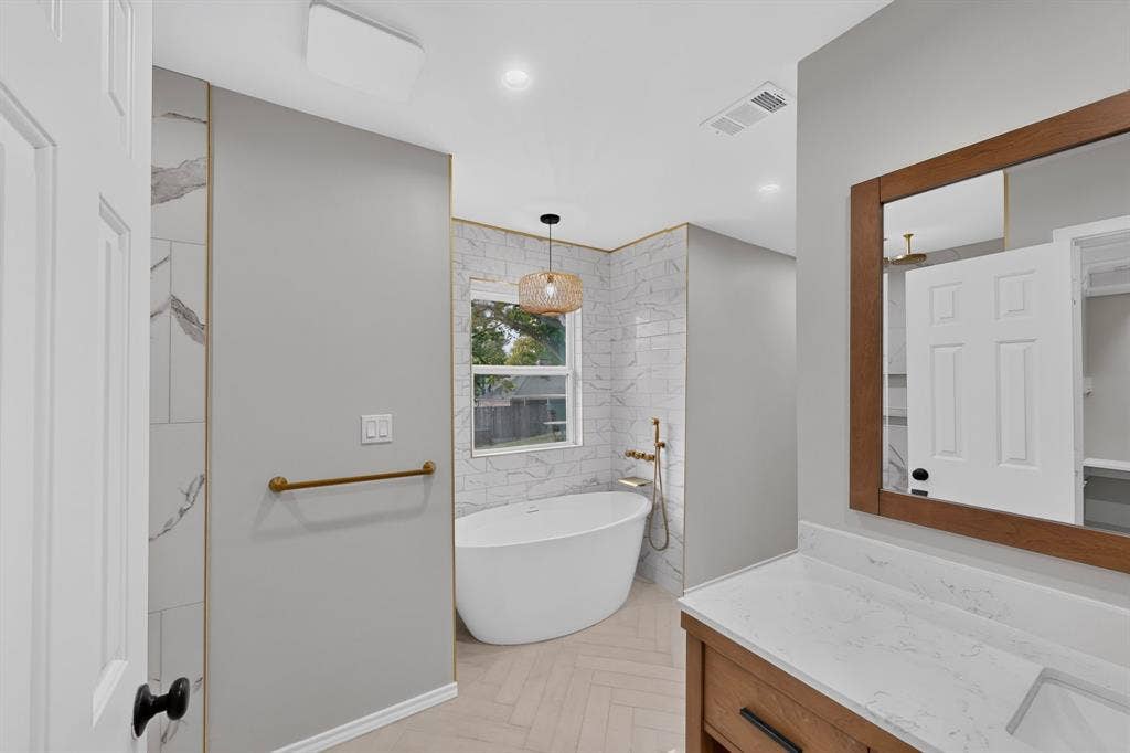 2413 Club Meadow Drive, Garland, TX 75041 Freestanding soaking tub with gold-tone fixtures, white subway tile wall surround, and wood-finish vanity with a single basin and white countertop