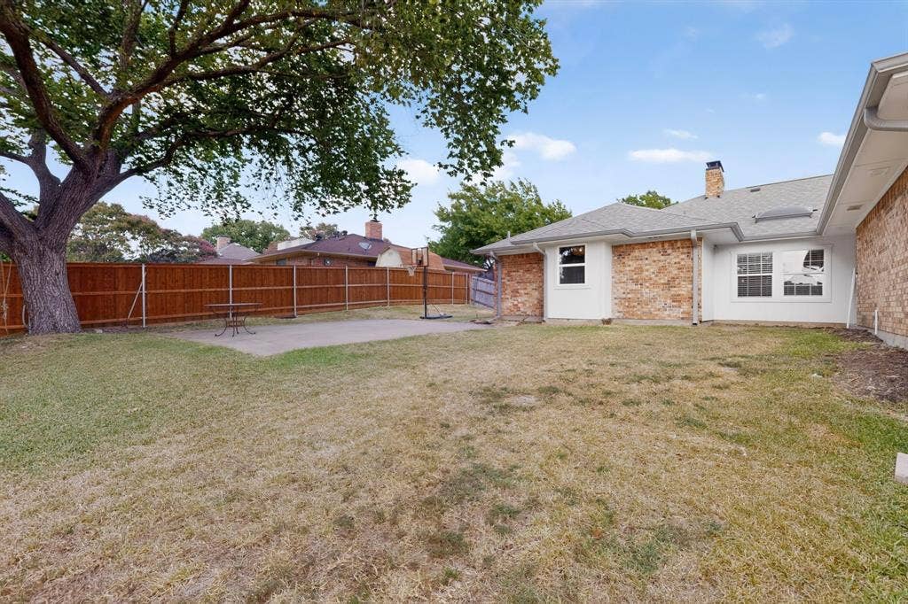 2413 Club Meadow Drive, Garland, TX 75041 Expansive backyard featuring a mature tree, privacy fencing, concrete patio, and brick exterior