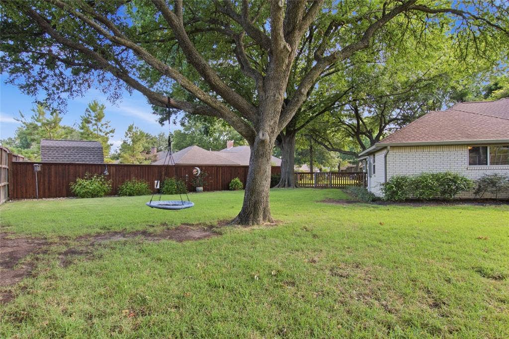 Expansive backyard featuring a mature canopy tree, wood privacy fencing, a brick-exterior home, and a storage shed
