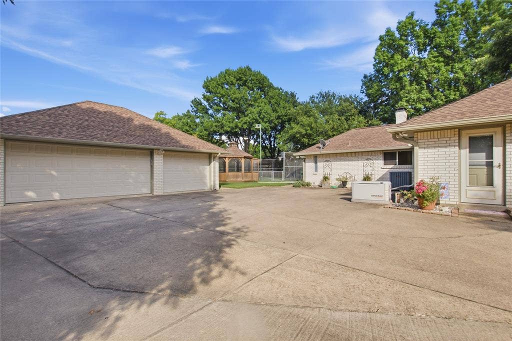 3 Car Detached Garage and motor court featuring a multi-car garage, brick exterior construction, roof-mounted generator, and a wood-frame gazebo
