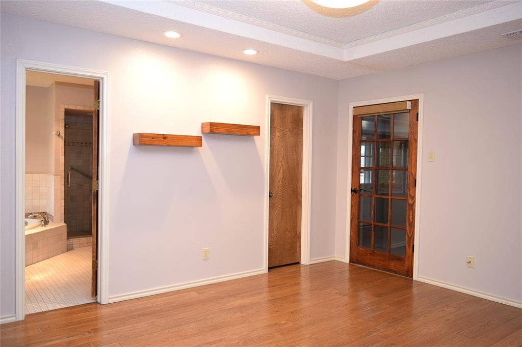 Tray ceiling featuring recessed lighting, wood-finish flooring, two natural wood floating shelves, and a solid-wood door with glass panes