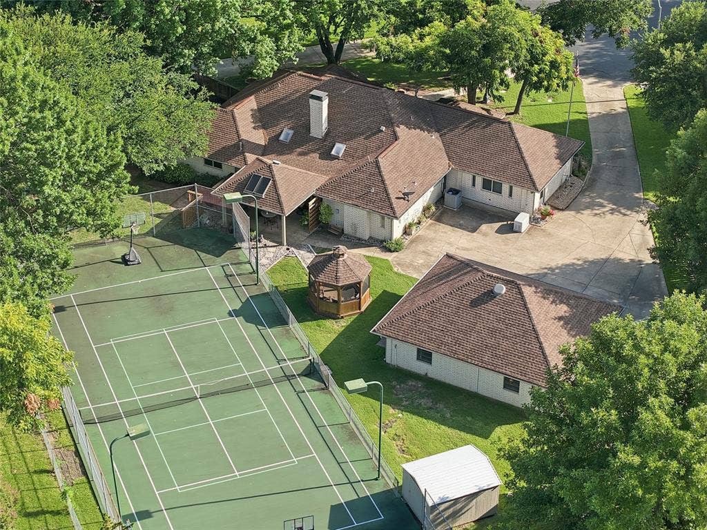 Aerial perspective featuring a hard-surfaced tennis court, detached garage, gazebo, concrete driveway, and sprawling tree-lined grounds