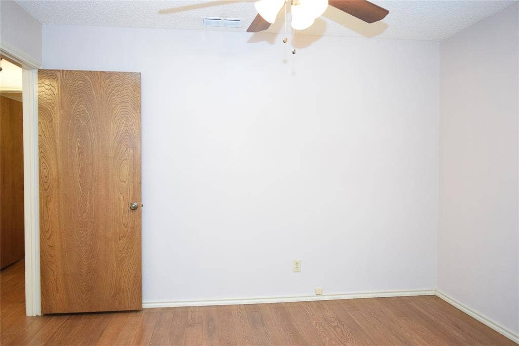 Neutral-toned interior space featuring wood-finish flooring, a solid wood-grain interior door, and a ceiling-mounted fan with integrated lighting