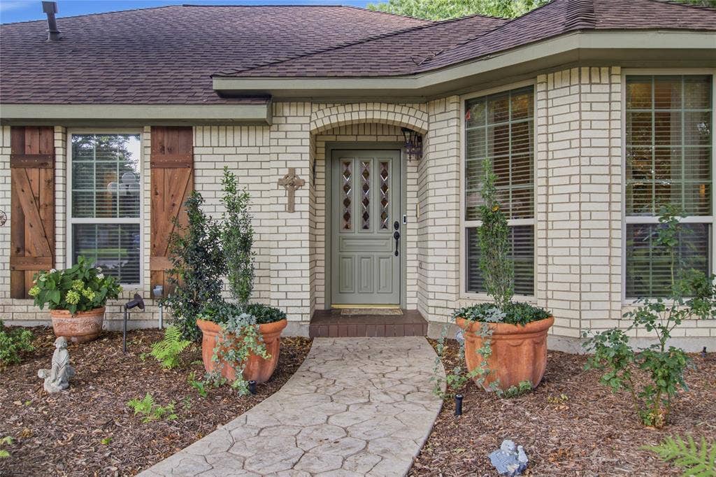 Light brick facade featuring decorative wood-finish shutters, a covered entryway, and a patterned concrete walkway