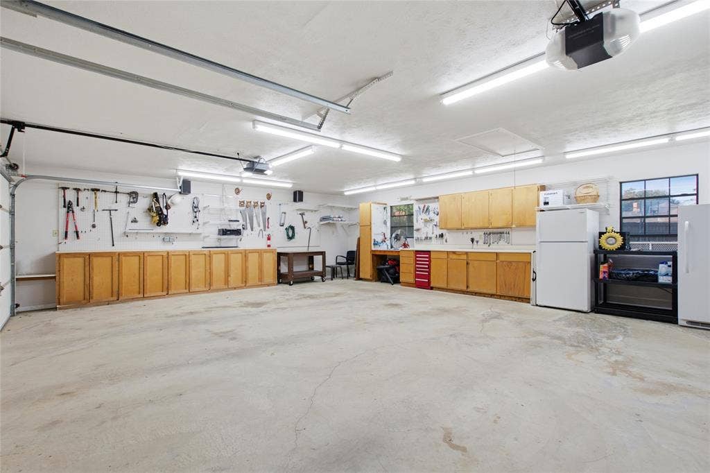 Spacious garage featuring extensive built-in wood-finish cabinetry, concrete flooring, overhead LED lighting, and a multi-pane window