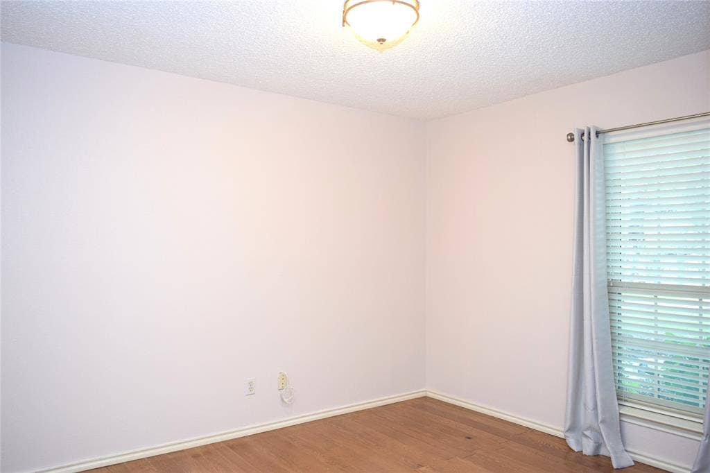 Room featuring wood-finish flooring, a neutral wall palette, a textured ceiling, and a window fitted with horizontal blinds