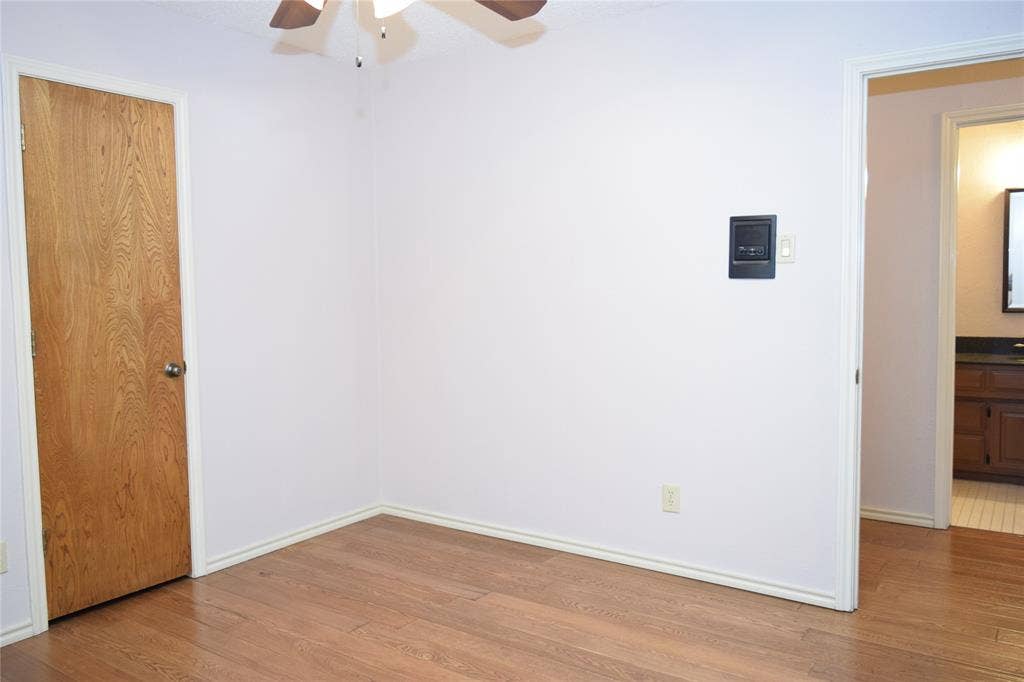 Room with wood-finish flooring, solid wood-finish door, and ceiling fan with integrated lighting
