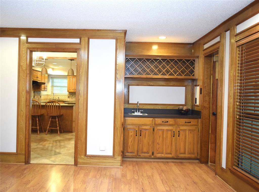 Custom built-in bar featuring wood cabinetry, integrated lattice wine storage, countertop, sink, and wood-finish flooring