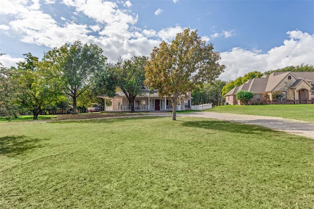 Expansive acreage featuring a wrap-around porch, mature shade trees, and a gravel driveway