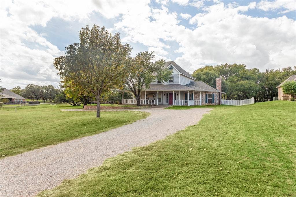 Two-story residence featuring a wraparound porch, exterior brick and siding facade, gravel driveway, and expansive lawn