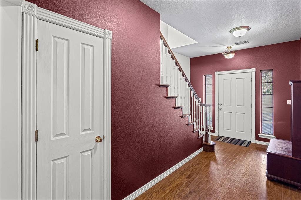 Foyer featuring wood-finish flooring, a staircase with white balusters, decorative door casing, and dual vertical sidelights flanking the entry door