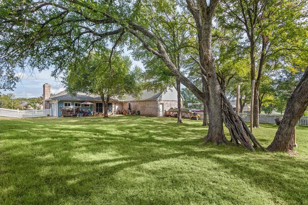 Expansive backyard featuring mature trees, a brick and siding exterior, a masonry chimney, and perimeter white picket fencing