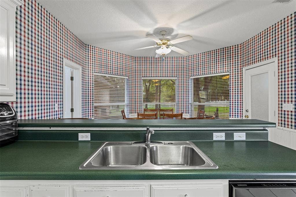 Kitchen area featuring a green solid-surface countertop with an undermount double-basin stainless steel sink, a bay window configuration, and a ceiling-mounted fan with integrated lighting