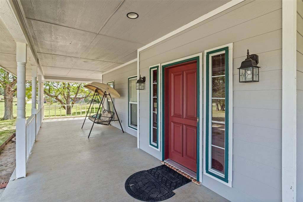 Covered front porch featuring lap siding, paneled front door with sidelights, and exterior wall-mounted lanterns