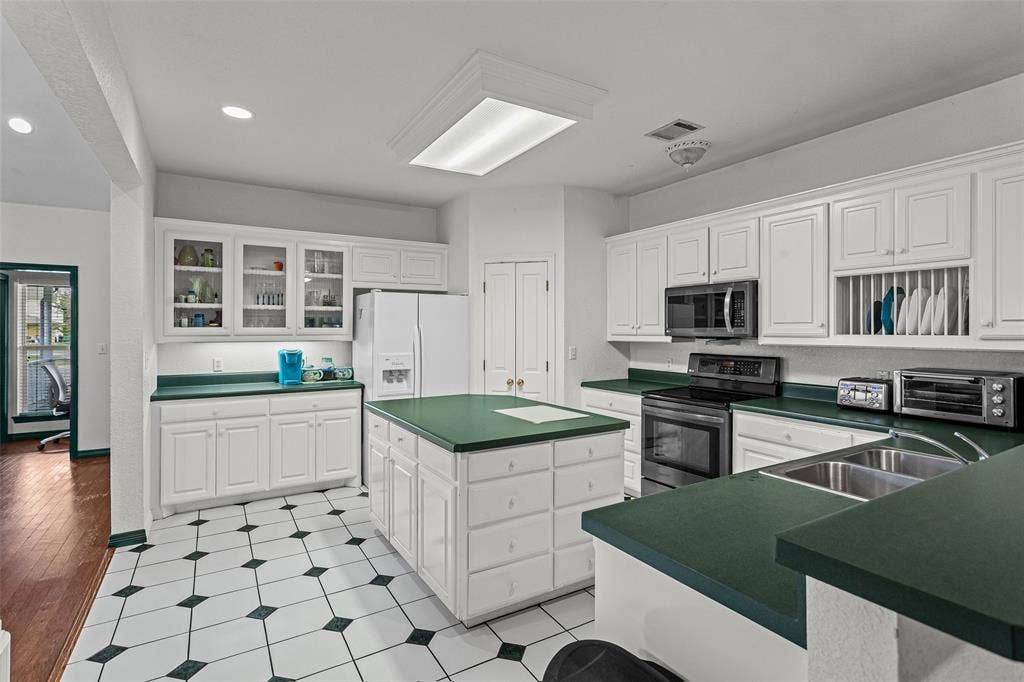 Kitchen featuring white cabinetry with glass-front display uppers, a central island with storage drawers, solid-surface countertops, and tile flooring