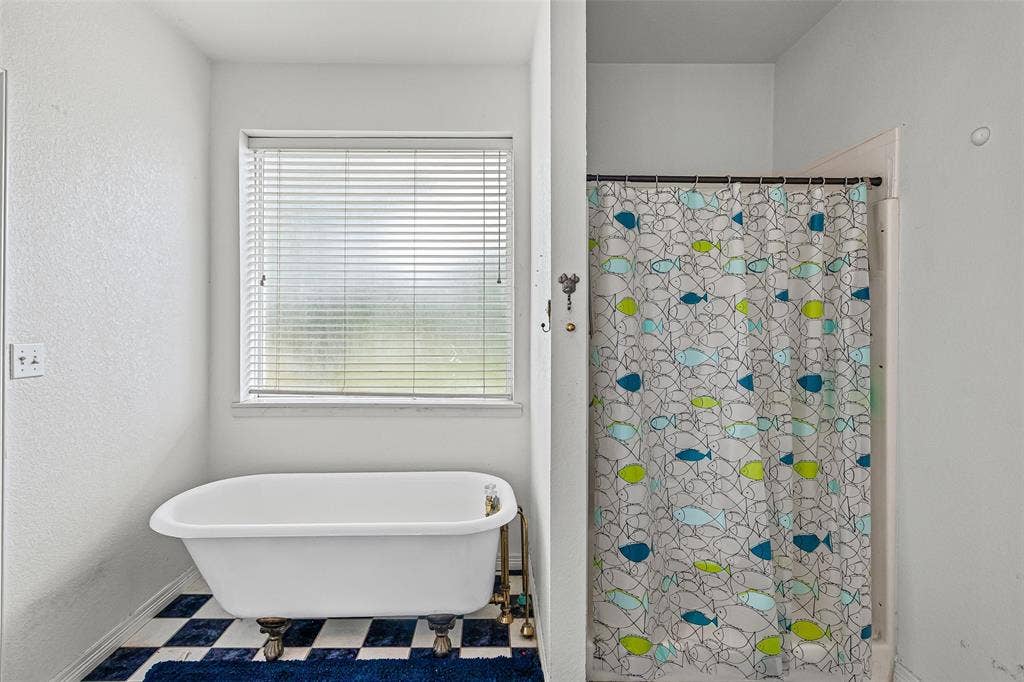 Freestanding clawfoot tub with metallic hardware, checkered tile flooring, and a window featuring horizontal blinds