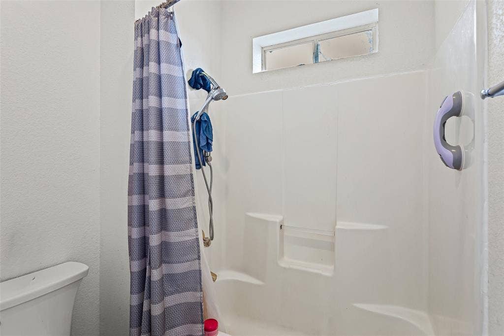 Bathroom featuring a one-piece molded tub and shower surround with built-in soap ledges, adjustable handheld shower fixture, and a transom window