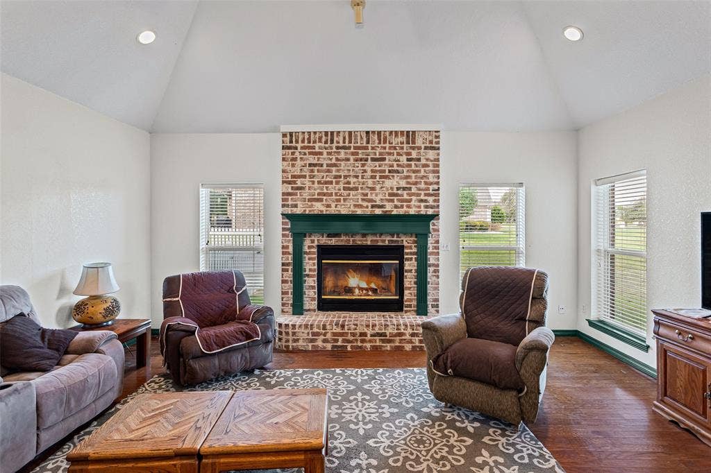 Vaulted ceiling with recessed lighting, brick fireplace, decorative mantel, wood-finish flooring, and multi-pane windows