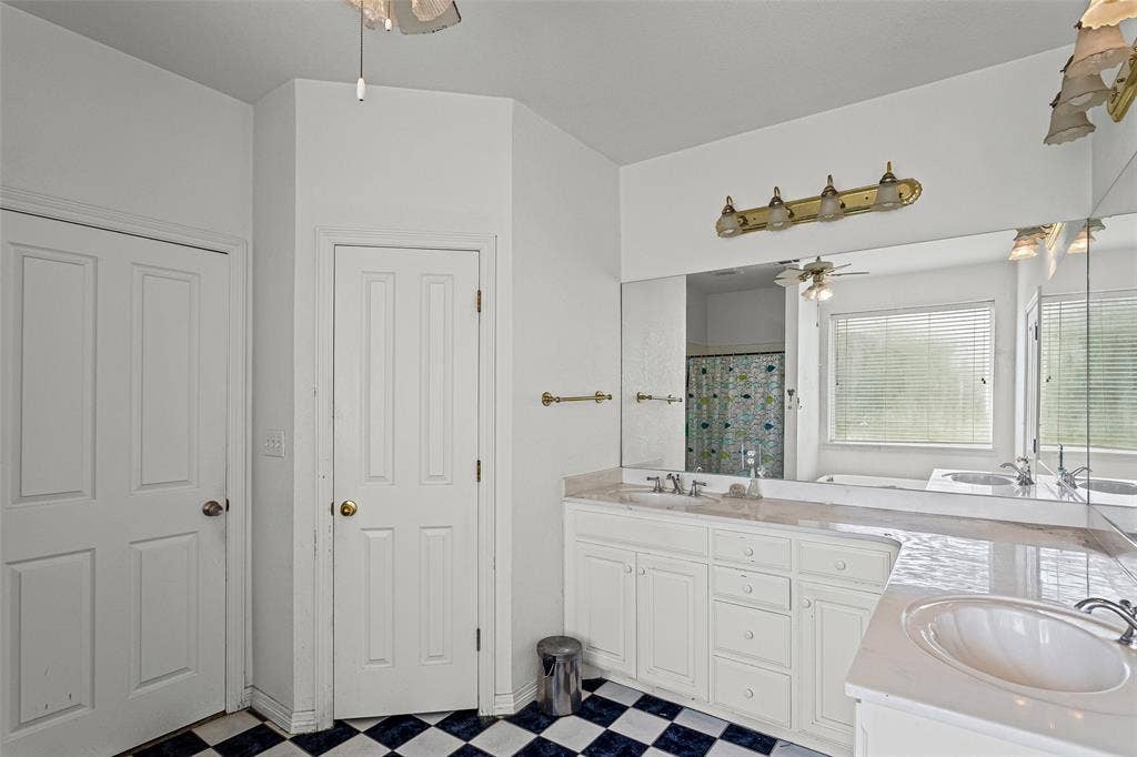 Dual-sink vanity with white cabinetry, expansive wall-to-wall mirror, multi-light vanity fixtures, and checkerboard patterned flooring