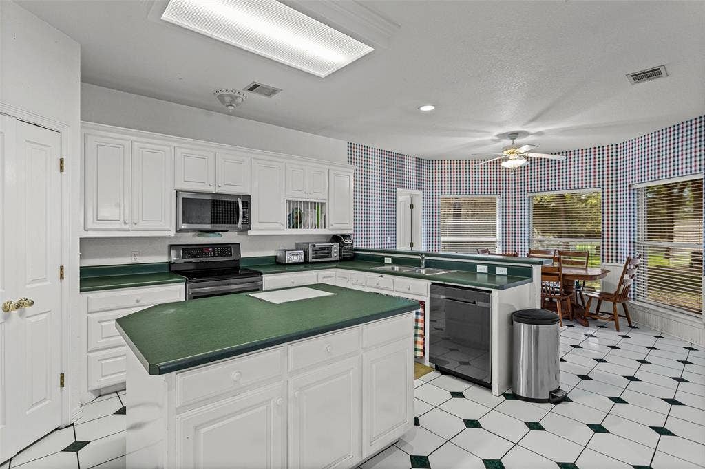 Kitchen featuring white cabinetry, a center island with solid surface countertops, stainless steel appliances, and checkered tile flooring